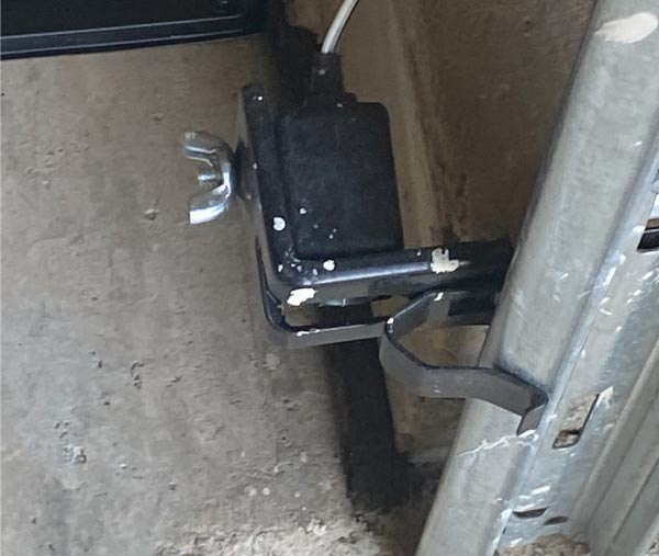 Close-up image showing a homeowner cleaning the dust and grime off the lens of a malfunctioning garage door safety sensor.